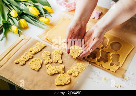 Frau schneidet Teig in Ostereierform, während sie Zuckerkekse macht. Backen im Urlaub. Draufsicht Stockfoto