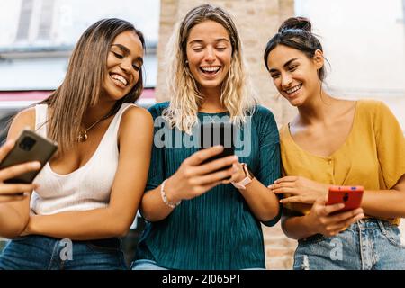 Lächelnde, multiethnische Freundinnen, die mit dem Mobiltelefon Spaß haben Stockfoto