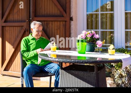 Älterer Mann, der an einem Frühlingstag auf der Veranda seines Hauses eine Limonade trinkt. Stockfoto