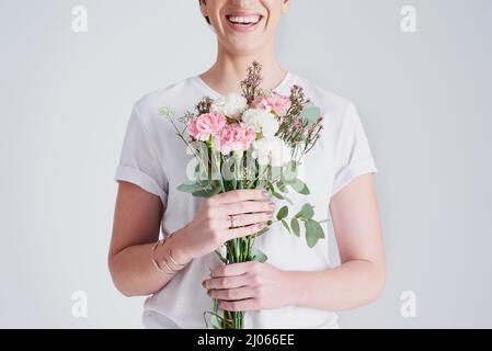 Glück kommt von Blumen. Studioaufnahme einer nicht erkennbaren Frau, die einen Blumenstrauß vor einem grauen Hintergrund hält. Stockfoto