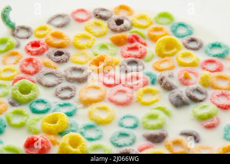 Vollkorn mehrfarbige Fruchtringe in Milch. Schnelles Frühstück mit Cerealien. Gesunde Ernährung. Gesunder Lebensstil. Hintergrund, Tapete, Textur. Banner, Adverti Stockfoto