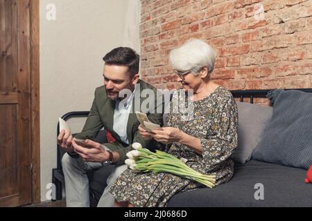 Ein hübscher Kaukasusmann und seine liebevolle, fröhliche Mutter, die alte Fotos ansieht. Hochwertige Fotos Stockfoto