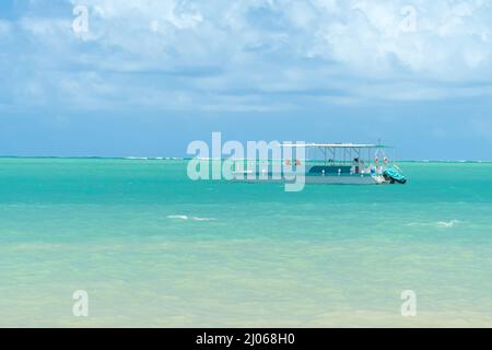 Touristenkatamaran, der an einem wunderschönen Strand mit türkisfarbenem Wasser festgemacht ist. Touristenkatamaran am Strand von Barra Grande, Maragogi - AL, Brasilien. Bootstour mit Koncep Stockfoto