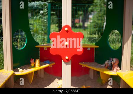 Details des Spielplatzes für Vorschulkinder. Kinderbereich auf der Straße. Rote Figur aus Brett auf Sandkasten fixiert. Platz für Kinder zum Entspannen im Sommer. Stockfoto