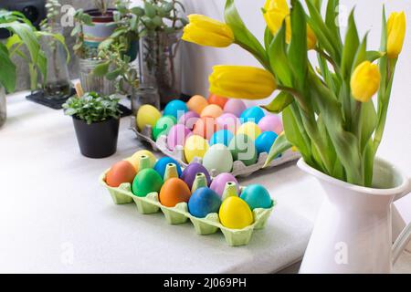 Viele bunte Ostereier in Kartonschachtel auf dem Tisch im Kücheninnenraum Stockfoto