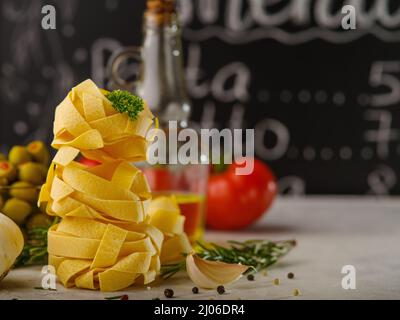 Kreative Komposition. Italienische Pasta, eine Flasche Olivenöl, Tomaten, Kräuter, Pfefferkörner auf schwarzem und weißem Hintergrund. Menügestaltung, gesundes Vegetar Stockfoto