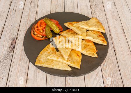 In Scheiben geschnittenes Matzokäse-Omelett mit Tomatenscheiben und Gurken auf einem hellen Holztisch Stockfoto