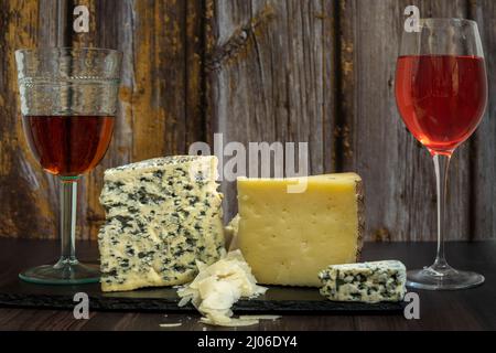 Stillleben mit einer Auswahl an salzigem Blauschimmelkäse, Brie-Käse, geräuchertem Manchego-Käse und ein paar Gläsern spanischem Roséwein Stockfoto