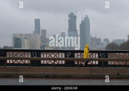 London, Großbritannien, 16.. März 2022. Eine Person geht über die Lambeth Bridge, während eine Staubwolke der Sahara Großbritannien erreicht. Am frühen Morgen nahm der Himmel über London ein unheimliches gelbes Aussehen an, und Regen während der Nachmittagsverkehrszeit brachte die Staubpartikel, die in Pfützen, auf Autos und auf Gehwegen zu sehen sind, zum Absinken. Kredit: Elfte Stunde Fotografie/Alamy Live Nachrichten Stockfoto