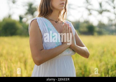 Die Schwangere steht mit grünem Gras auf dem Feld und faltet ihre Hände im Gebet. Sonnenschein, sommerliche Stimmung Stockfoto