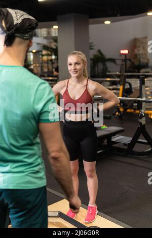 Ein von einem Trainer geleitete Training hilft einem schönen Kunden, Übungen in einem Fitnessclub durchzuführen, das Konzept des Sportens mit einer professionellen Fitnessleisure Stockfoto