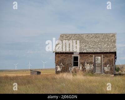 Verlassene Bauernhaus mit Windturbinen im Hintergrund und hohes Gras im Vordergrund. Das Bild verfügt über Kopierspeicher. Stockfoto