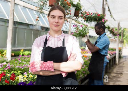 Junge erfahrene Mitarbeiterin im Garten arbeiten im Gewächshaus, Kontrolle der Blumen Stockfoto