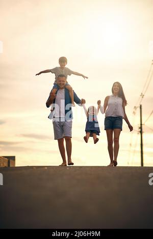 Wir lieben es, uns über lange Spaziergänge zu verbinden. Aufnahme einer jungen Familie, die draußen die Straße entlang spazieren geht. Stockfoto