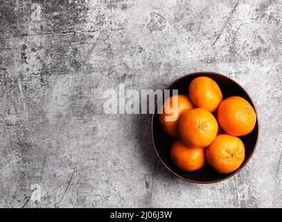 Mandarinen in einer Schüssel auf dunkelgrauem Hintergrund. Draufsicht, flach liegend Stockfoto
