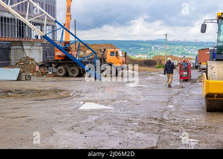 Eine Baustelle mit einer temporären Straße, die mit Betonplatten gesäumt ist, auf der sich ein LKW-Kran und Straßenausrüstung befinden, in der Ferne Haufen von Lehm Stockfoto