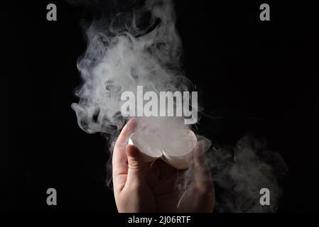 Rauch kommt aus einem zerbrochenen Ei in den weiblichen Händen. Stockfoto