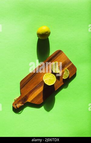 Zitronenlime auf einem grünen Hintergrund auf einem Holzbrett mit markierten Schatten gespalten Stockfoto