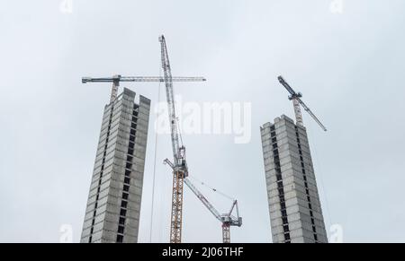 Zwei indentische Skyscrapper im Konstruktionsprozess, aus Betonplatten. Baustelle mit mehreren Turmdrehkranen und unfertigen Bui Stockfoto