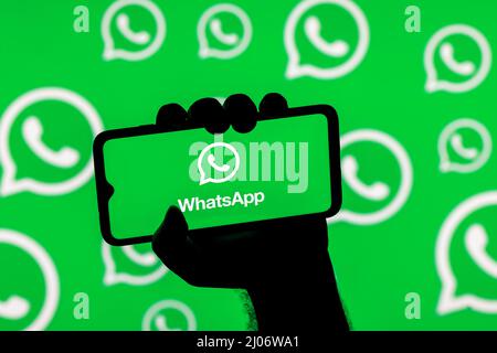 Smartphone mit dem Whatsapp Messenger auf dem Bildschirm in einer geballten Hand auf dem Hintergrund der Whatsapp Logos Stockfoto