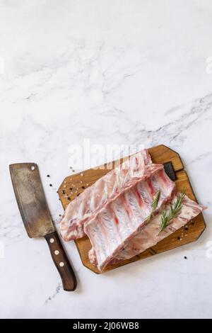Rohes Kalbsbriketts Fleisch mit Rosmarin und Gewürzen auf kurzen Rippen zum Kochen auf Marmorplatte. Draufsicht, flach liegend. Speicherplatz kopieren. Stockfoto