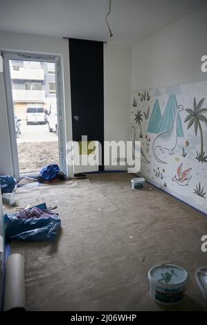 Kinder spielen in einem renovierten Zimmer mit Dinosaurierzeichnungen an der Wand in einem Apartment Stockfoto