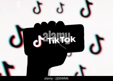 Smartphone mit dem Logo des sozialen Netzwerks TikTok auf dem Bildschirm in einer zusammengeballten Hand auf dem Hintergrund der TikTok-Logos Stockfoto