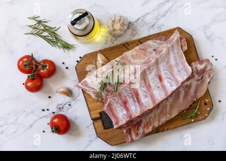 Rohes Kalbsbriketts Fleisch mit Gemüse und Gewürzen auf kurzen Rippen zum Kochen auf Marmorplatte. Draufsicht, flach liegend. Stockfoto