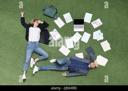 Mitarbeiter lagen müde auf Gras, erschöpfte Mitarbeiter mit Papieren und Geschäftsunterlagen umgeben Stockfoto