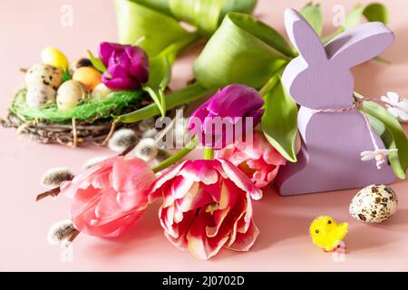 Rosa und lila Tulpen mit bunten Wachteleiern in einem Nest auf rosa Hintergrund. Konzept für Frühlings- und Osterferien. Stockfoto