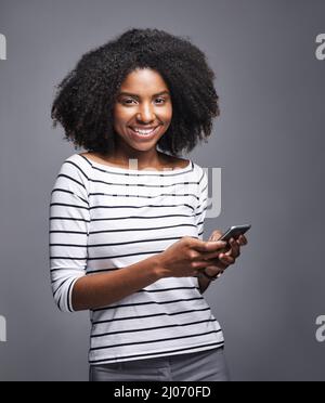 Ich muss mit jemandem sprechen, der mich auf meinem Handy erwischt. Studioporträt einer jungen Frau, die ein Mobiltelefon vor grauem Hintergrund benutzt. Stockfoto