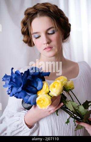 Porträt des kaukasischen ukrainischen Mädchens in weißem Kleid und gelb-blauen Blumen auf weißem Hintergrund. Die ruhige Dame schläft. Konzept - Stoppt den Krieg in der Ukraine. Stockfoto