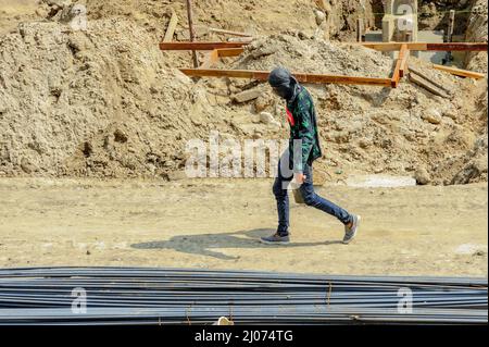 Ein Bauarbeiter auf der Baustelle, der einen Eimer voller Sand trägt, geht in der sengenden Sonne hastig spazieren. Stockfoto