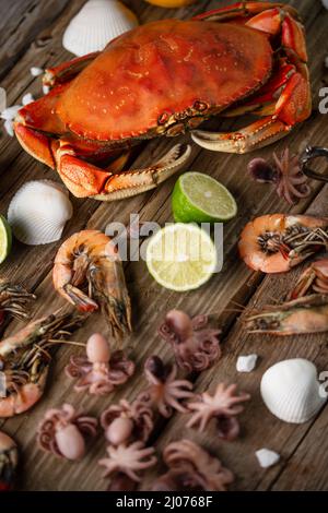 Blick von oben auf verschiedene Meeresfrüchte, serviert mit Gewürzen auf rustikalem Holzhintergrund. Gekochte Krabben, Garnelen und Babyoktopusse zum Abendessen. Meeresfrüchtekonzept. Stockfoto