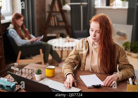 Horizontale Aufnahme von zwei jungen Frauen, die zu Hause im Internet studieren und surfen, im Vordergrund Stockfoto