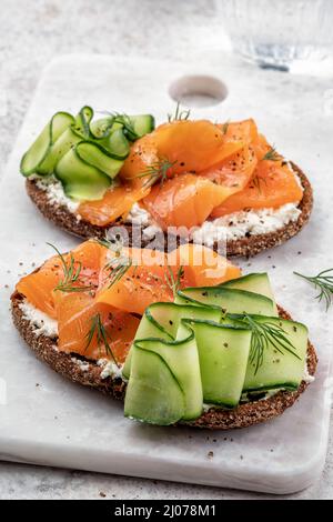Roggenbrot öffnet Sandwiches mit gesalzenem Lachs und Gurke auf einem Tisch aus weißem Stein. Gesunde Ernährung. Stockfoto