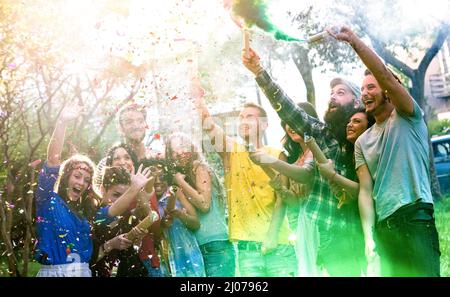 Glückliche Millennial-Freunde, die sich auf der Gartenparty mit bunten Rauchbomben draußen amüsieren - Junge Millennial-Studenten feiern Frühlingsferien fest tog Stockfoto