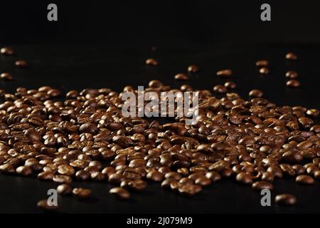 Verstreute, glänzend geröstete Kaffeebohnen auf schwarzem Hintergrund mit Platz für Kopien. Geringe Schärfentiefe Stockfoto