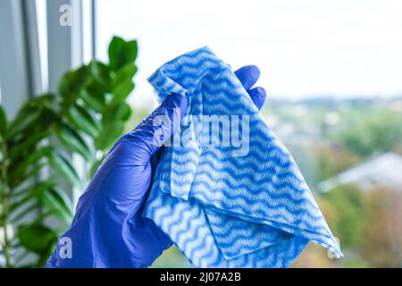Der Mitarbeiter hält einen Gummischutzhandschuh, der schmutziges Mikrofasertuch hält und das Fenster vom Staub abwischt. Allgemeine Frühjahrsputz. Hausarbeit und Housekeeping Stockfoto