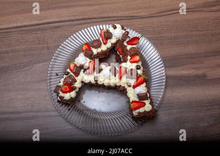 Kuchen in Form des Buchstabens A. Geburtstagskuchen mit Erdbeere und Schokolade. Kuchen mit Schlagsahne und Holzhintergrund. Stockfoto