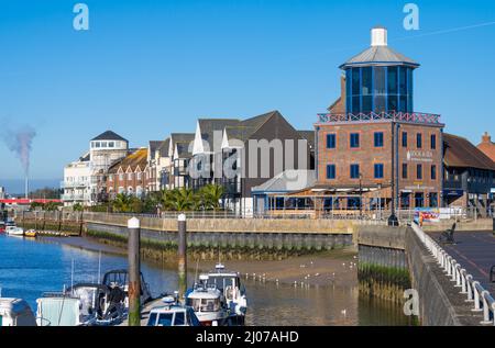 Blick auf die Häuser am Flussufer und das Besucherzentrum von Look & Sea mit Booten, die auf einem Ponton am Fluss Arun in Littlehampton, West Sussex, Großbritannien, festgemacht sind. Stockfoto