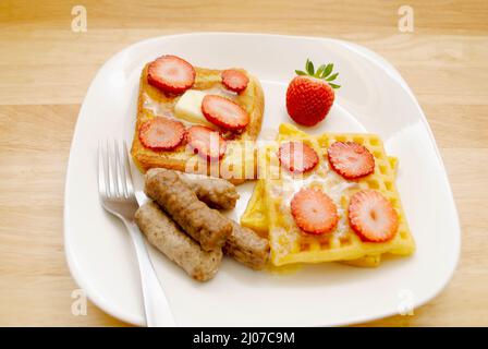Französischer Toast, Waffeln mit Ahornsirup und in Scheiben geschnittene Erdbeeren mit drei Schweinswurst-Links auf einem weißen Teller Stockfoto