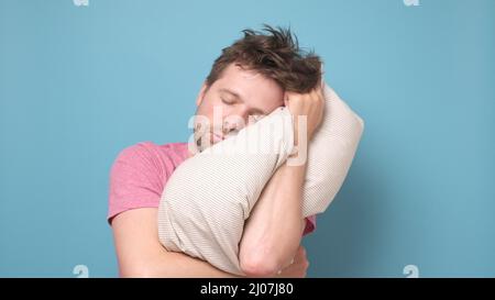 Der kaukasische junge Mann ist müde und sehr müde, wenn er sein Kopfkissen auf dem Kopf hält. Stockfoto