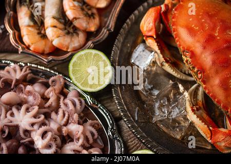 Makroansicht von Tellern mit verschiedenen Meeresfrüchten, serviert mit Gewürzen auf rustikalem Holzhintergrund. Gekochte Krabben, Garnelen und Babyoktopusse zum Abendessen. Se Stockfoto