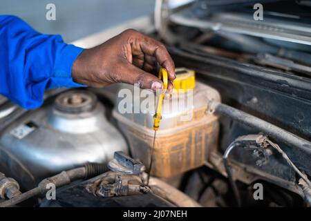 Nahaufnahme der Hände des Automechanikers, die den Motorölstand des Autos in der Garage prüfen - Konzept für Wartungsservice, Blaukragenarbeiten und Schmiermittel Stockfoto