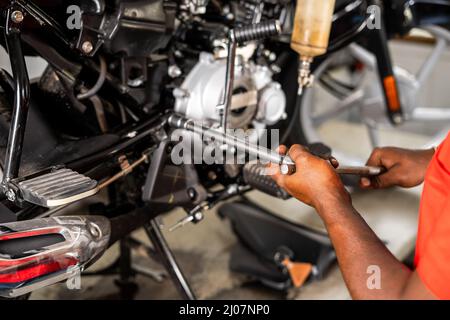 Schulteraufnahme des Fokus auf die Hände, Motorrad-Mechaniker Befestigung oder Reparatur Motor in der Garage - Konzept der Wartung und Beruf. Stockfoto