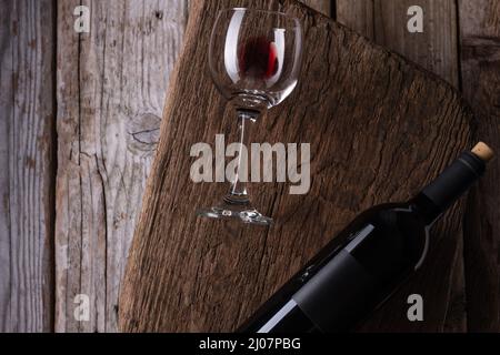 Makro-Aufnahme aus Glas mit Resten von Rotwein und dunkel elegante Flasche auf Holzbrett auf rustikalem Hintergrund. Werbe- und Promotion-Konzept. Modell. Stockfoto