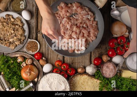 Chef Hände Salze Braten Hähnchenfilet in der Pfanne für die Vorbereitung Füllung auf Holztisch mit verschiedenen Zutaten Hintergrund. Konzept des Kochens pro Stockfoto