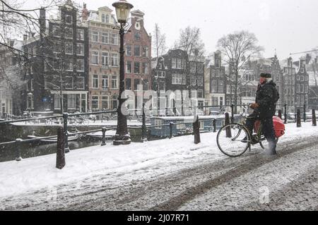 Reifer Mann auf seinem Fahrrad, der über den fallenden Schnee nachdenkt, im Jordaan-Viertel, Amsterdam, Niederlande Stockfoto