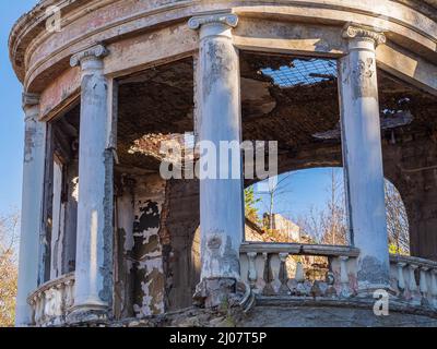 Halbrunde Fragmente von verlassenen Restaurant ruiniert mit Säulen und Balustern im griechischen Stil, überwuchert mit Bäumen und mit einem kaputten Dach Stockfoto